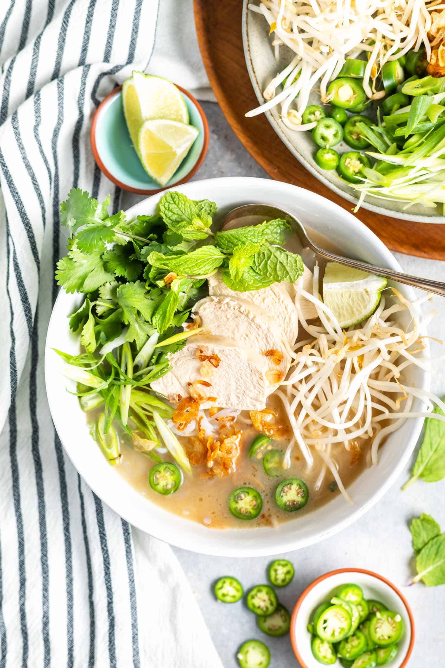 Keto Vietnamese Chicken Noodle Soup in bowl with a plate of toppings to the side