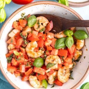 Grilled Shrimp Bruschetta in a bowl with a wooden spoon, there is a tomato in the background