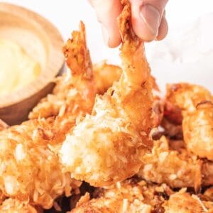 A hand picking up a single coconut shrimp from the serving tray