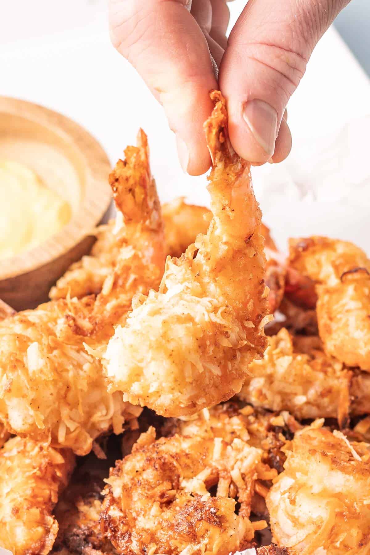 A hand picking up a single coconut shrimp from the serving tray