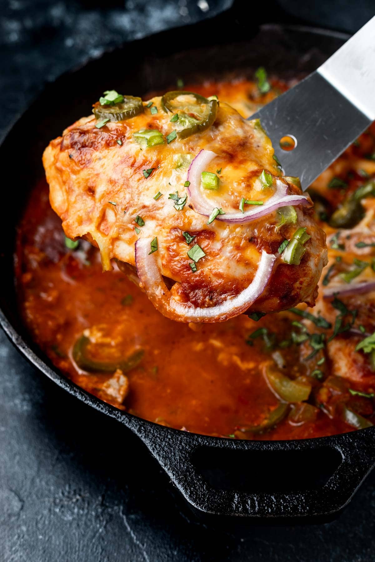 Keto BBQ Chicken Bake, a piece of baked chicken being scooped out of a cast iron skillet