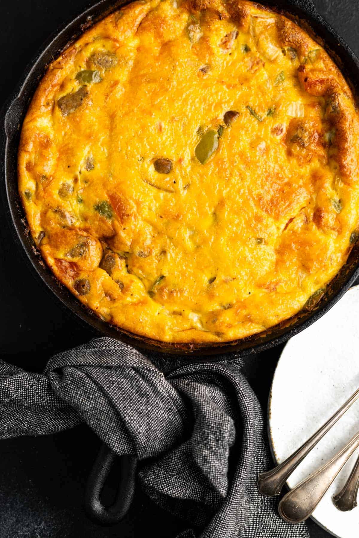 Keto Breakfast Casserole in a cast iron skillet with two white plates and forks sitting beside it.