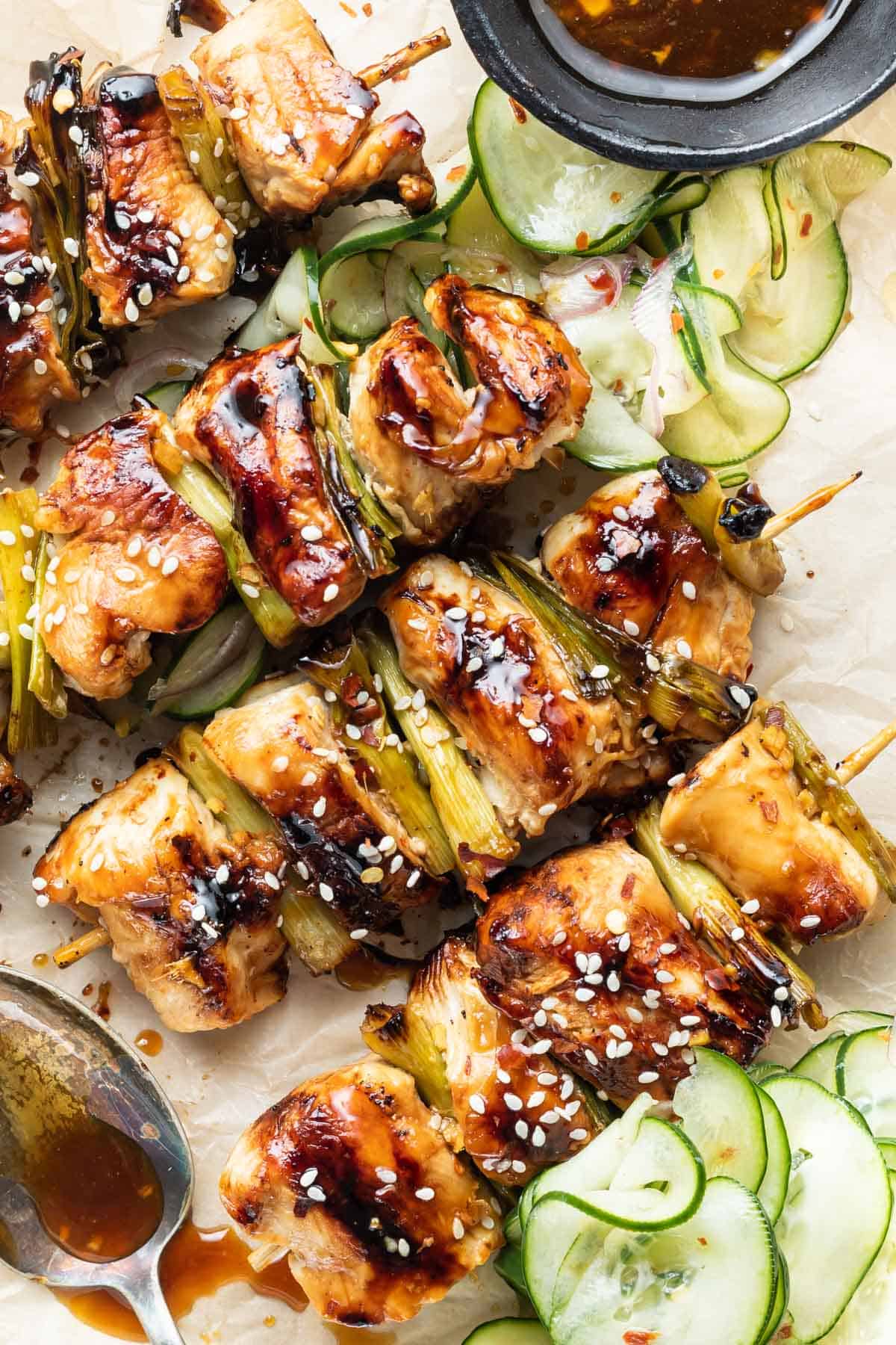 Keto Chicken Teriyaki Skewers with Pickled Cucumber Salad on a tray with a spoon splattering sauce over the top