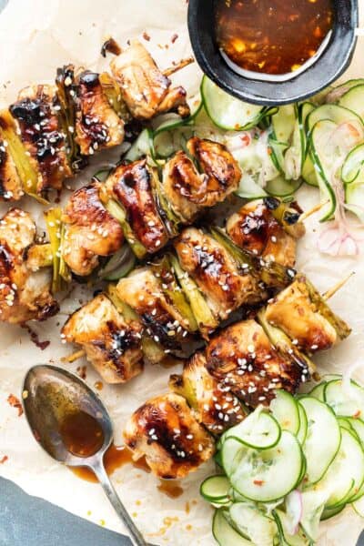 Keto Chicken Teriyaki Skewers with Pickled Cucumber Salad on a tray with a spoon splattering sauce over the top