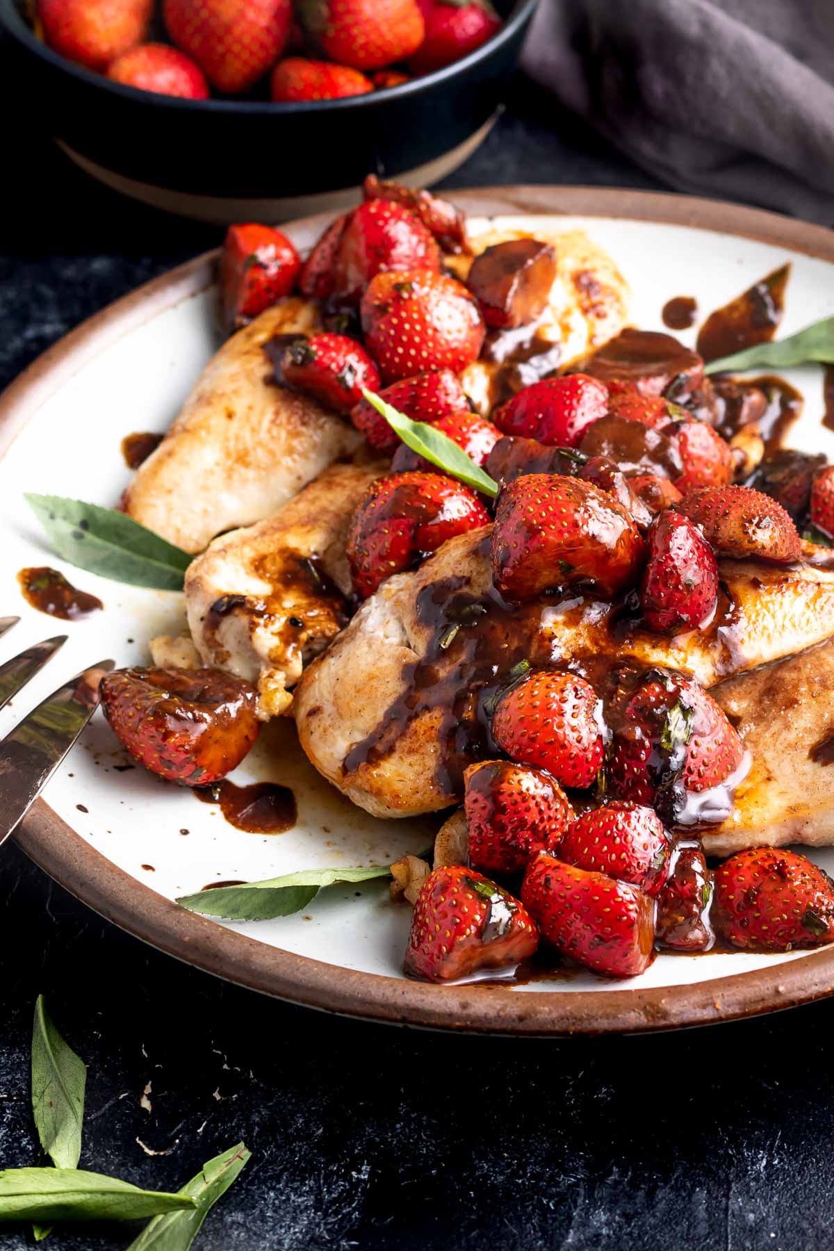 Strawberry Balsamic Tarragon Chicken on a plate with a bowl of strawberries in the background