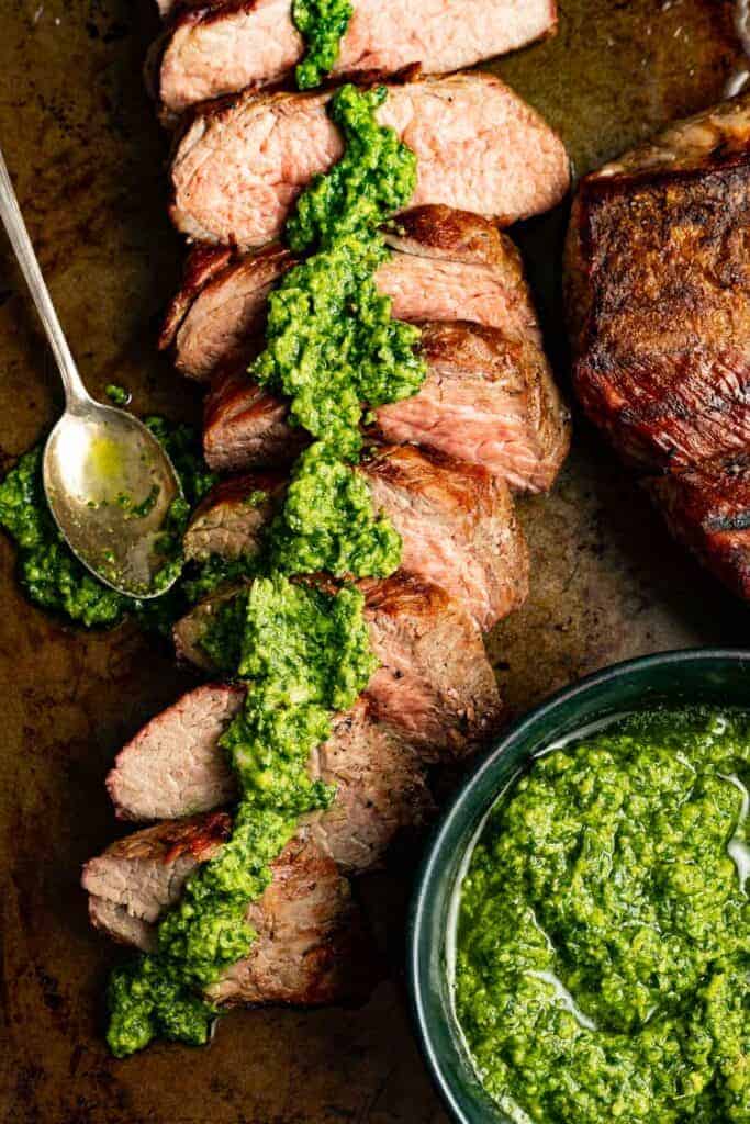 sliced tri-tip steak on a platter drizzled with creamy avocado chimichurri