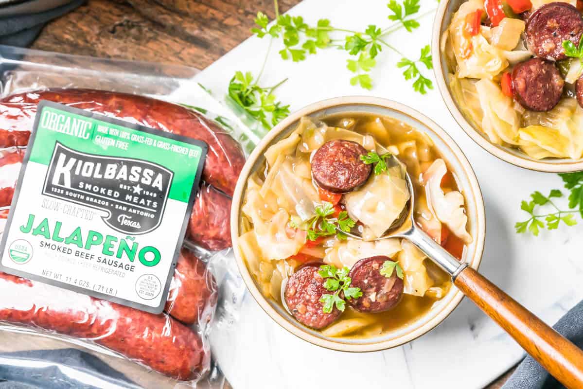 Keto Cabbage Soup in a bowl with a package of Kiolbassa smoked sausages sitting next to it