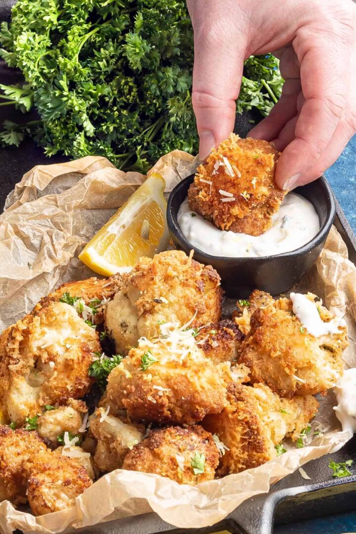 Keto Italian Cauliflower Poppers on a black cast iron tray with one being dunked into a sauce