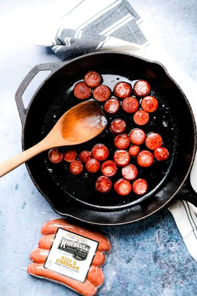 browning smoked sausage rounds in a cast-iron skillet