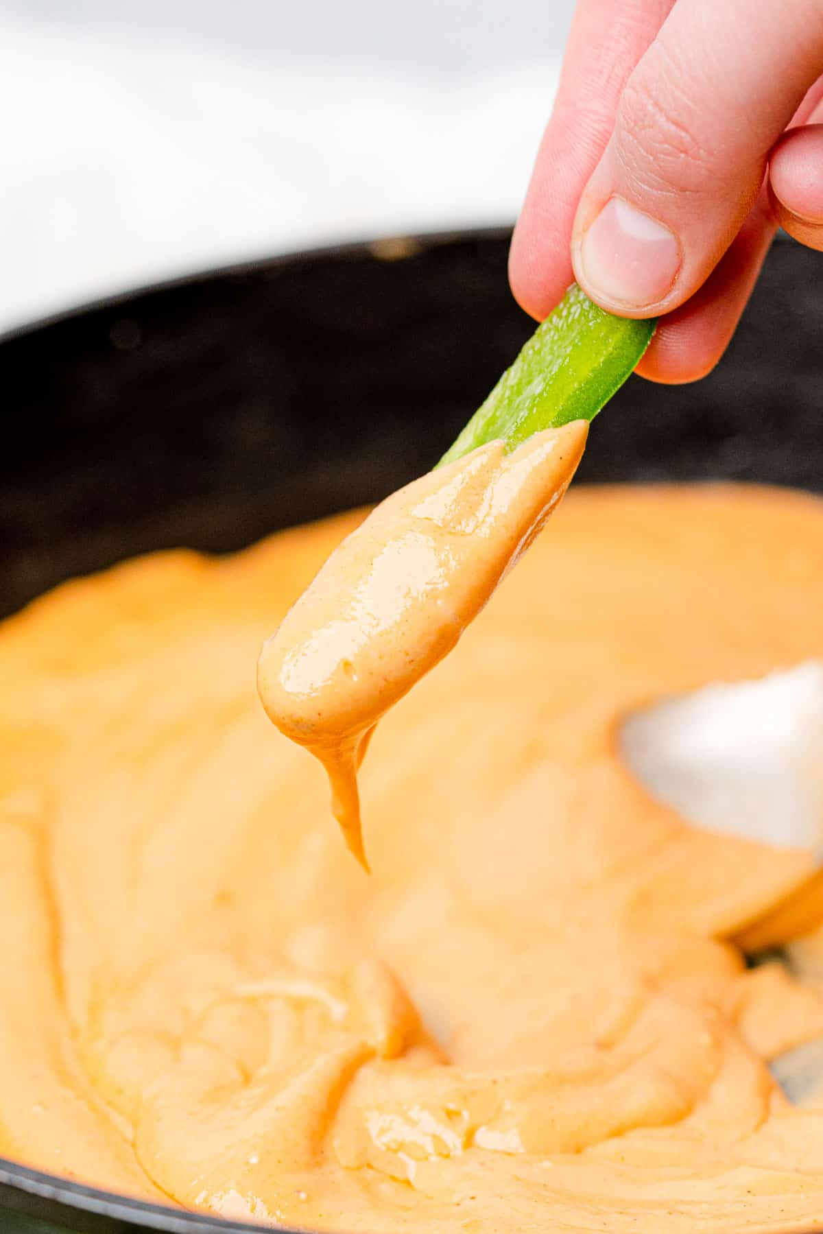 a bell pepper strip being dunked into cheddar cheese sauce