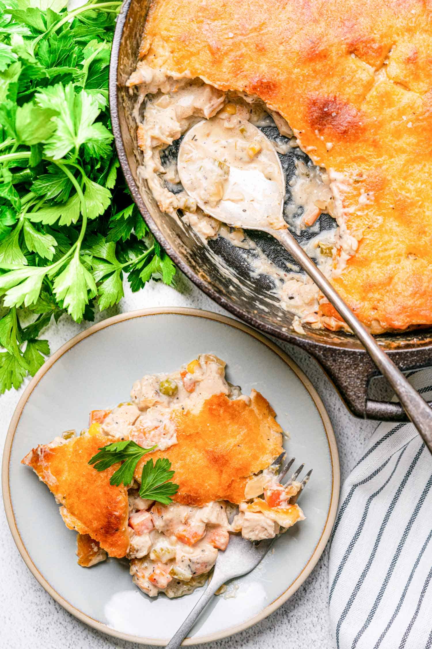 Keto Chicken Pot Pie in a cast iron skillet with a spoon taking a serving out and a plate to the side with a serving on it