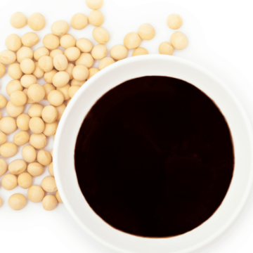 soy sauce in a white bowl on a white background with soybeans scattered around