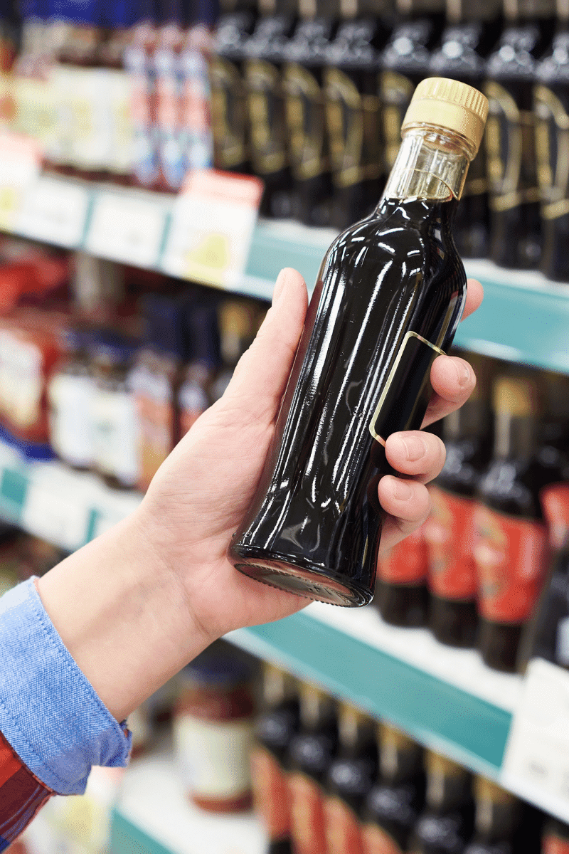 a hand holding a bottle of soy sauce in a grocery store