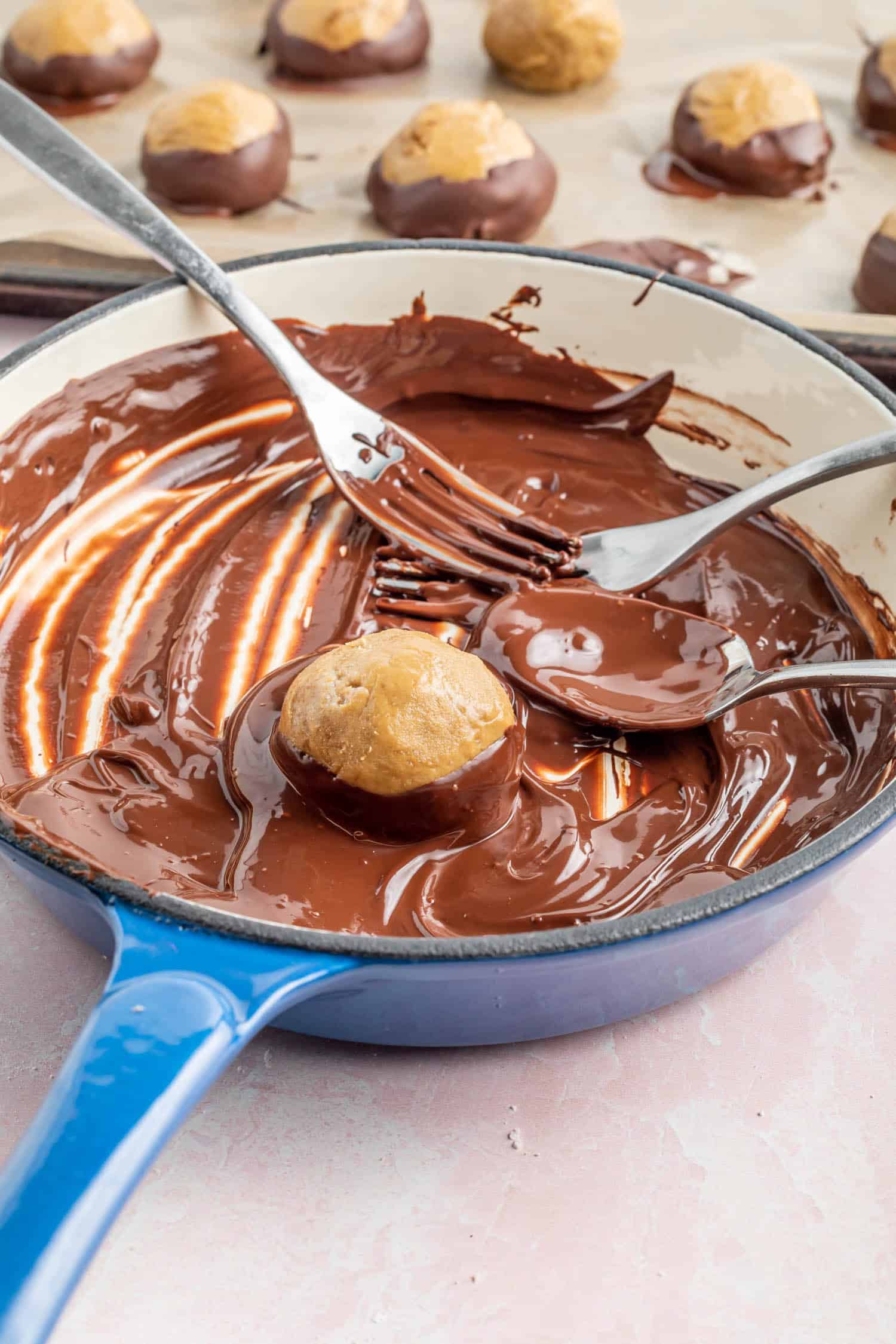 melted chocolate in a enameled cast iron skillet, dipping a buckeye ball into the chocolate