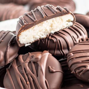 Keto Peppermint Patties in a bowl stacked on top of each other. One is cut in half showing the creamy white center.,