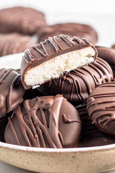 Keto Peppermint Patties in a bowl stacked on top of each other. One is cut in half showing the creamy white center.,