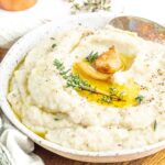 keto mashed cauliflower in a white bowl topped with roasted garlic and thyme