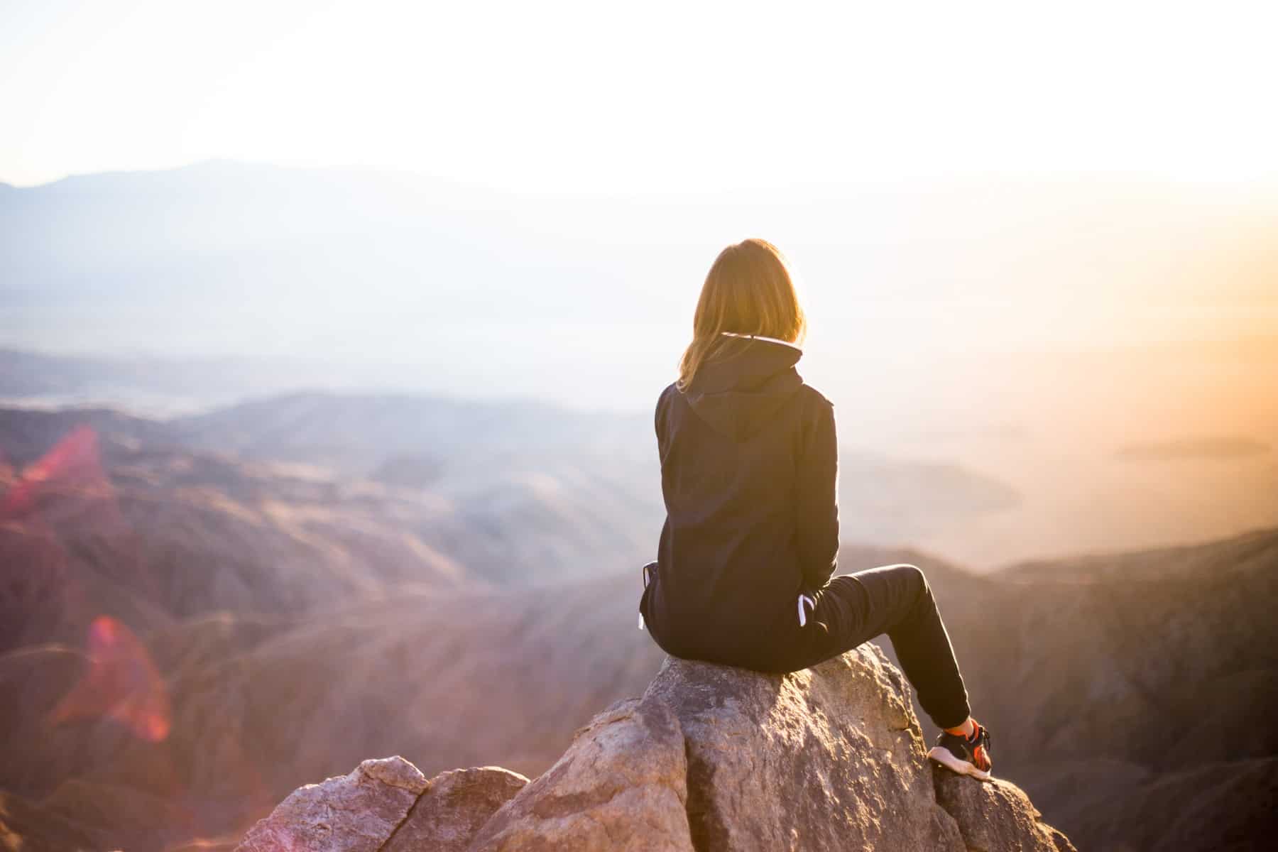 a woman sitting on top of a rock overlooking a canyon