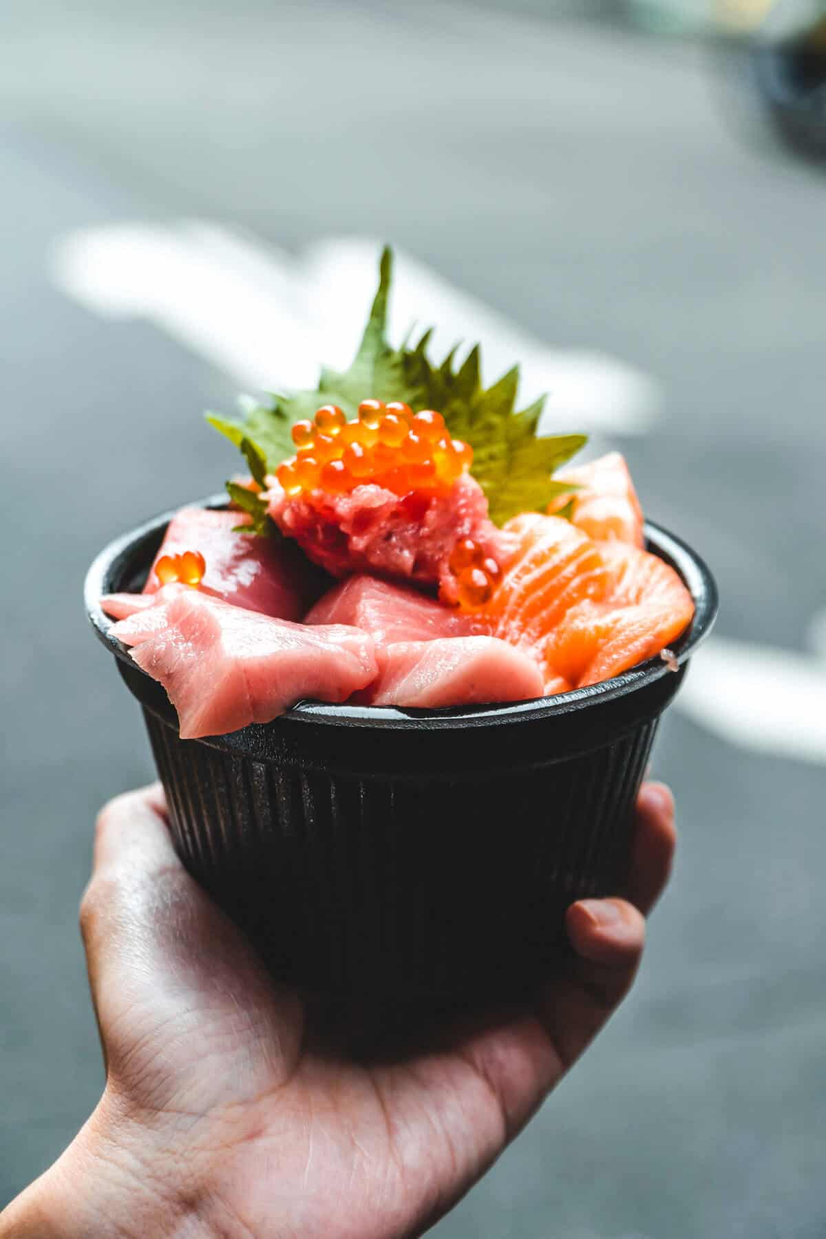 a hand holding bowl of raw fish