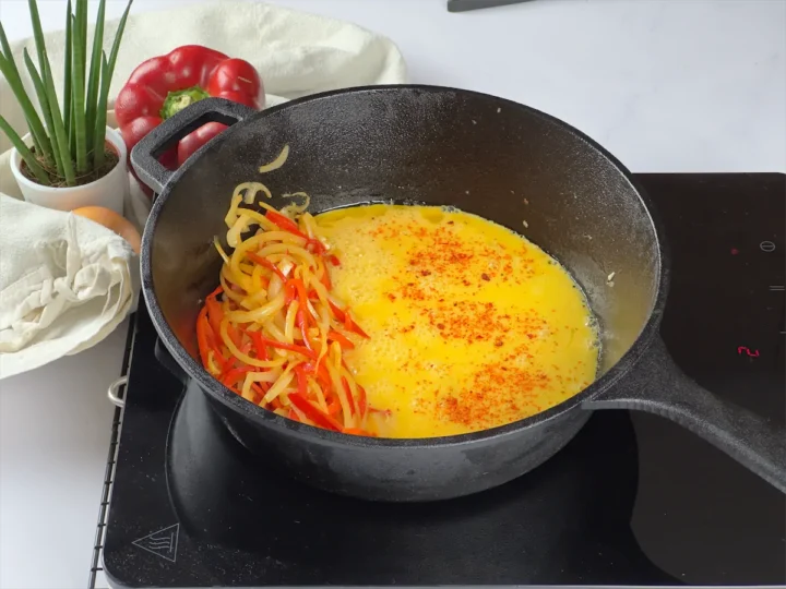 Egg mixture in a skillet with slices of cooked bell peppers and onions.