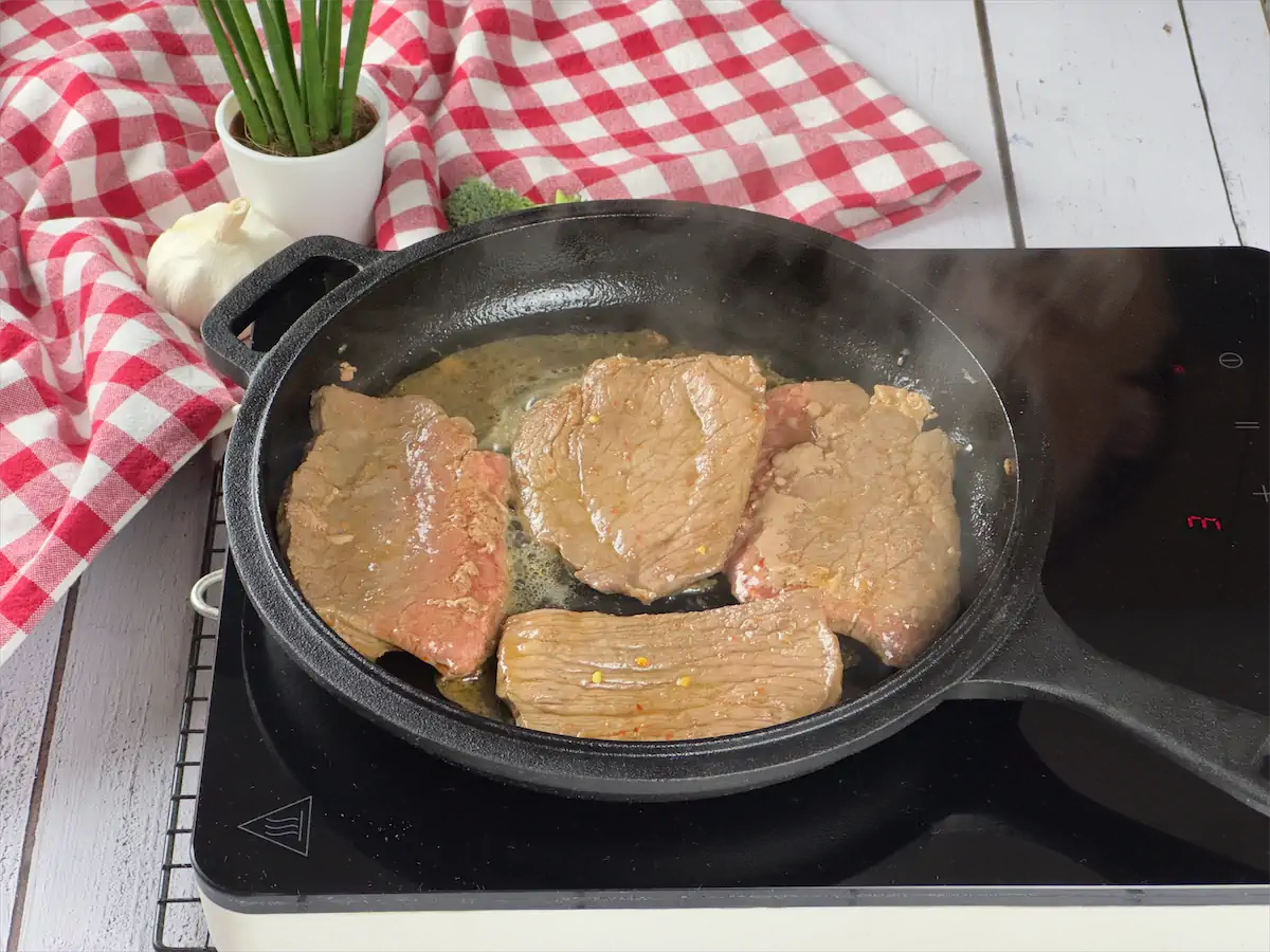 Frying beef pieces in a cast iron pan.