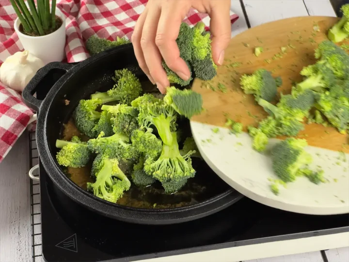Transferring broccoli from a plate to a cast iron skillet.