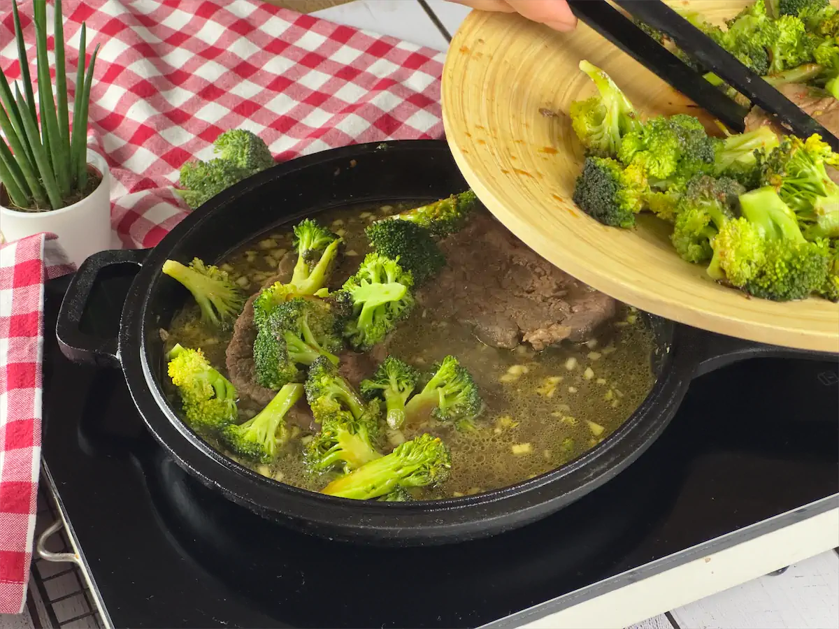 Transferring beef and broccoli in chicken broth in a cast iron skillet.