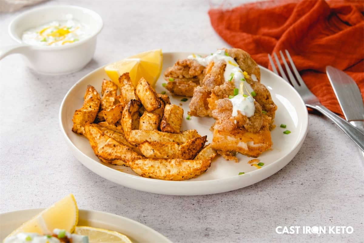 a white plate topped with fried keto-friendly fish and chips next to a bowl of dipping sauce.