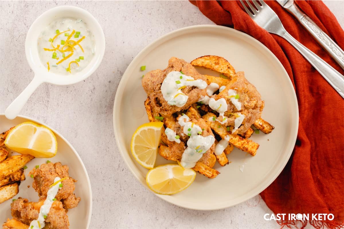 a white plate topped with keto-friendly fish and chips next to a bowl of sauce.