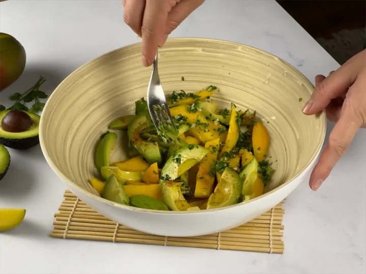 Using a fork to mash mango and avocado slices and other ingredients.