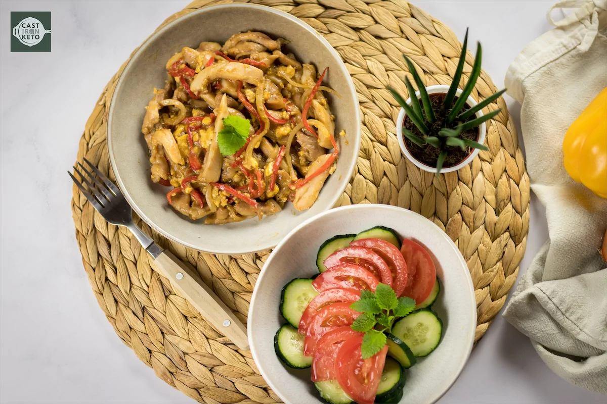 Overhead shot of Keto Pad Thai served in a bowl, alongside another bowl full of sliced sliced cucumber and tomatoes.