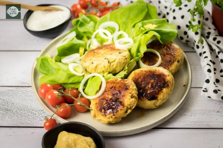 Keto-friendly turkey burger patties resting on fresh lettuce, surrounded by colorful vegetable garnishes.