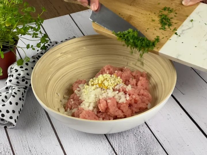 Parsley being added to a bowl with ground turkey, chopped onions, Dijon mustard, and minced garlic.