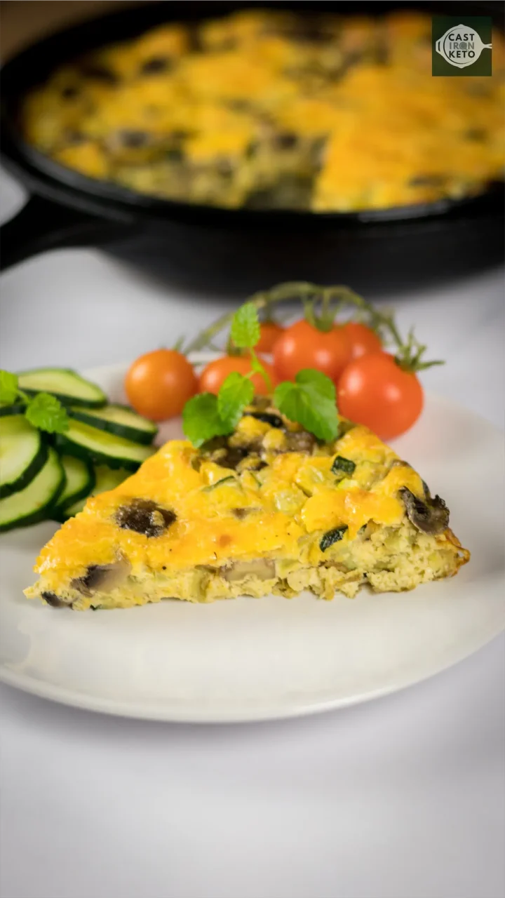 Keto Vegetable Frittata piece served on a white plate alongside red cherry tomatoes and sliced cucumber.