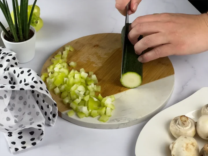 Zucchini on a chopping board being sliced by a sharp knife.