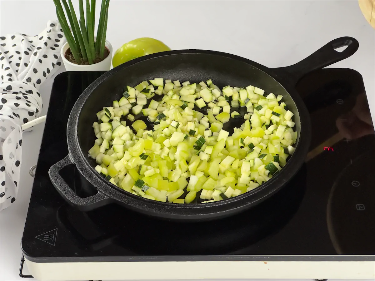 Vegetables being sautéed in a cast iron pan placed on an induction stove.