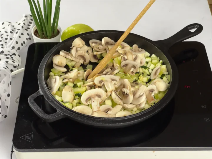 Vegetables on a cast iron pan being sautéed by a wooden spatula.