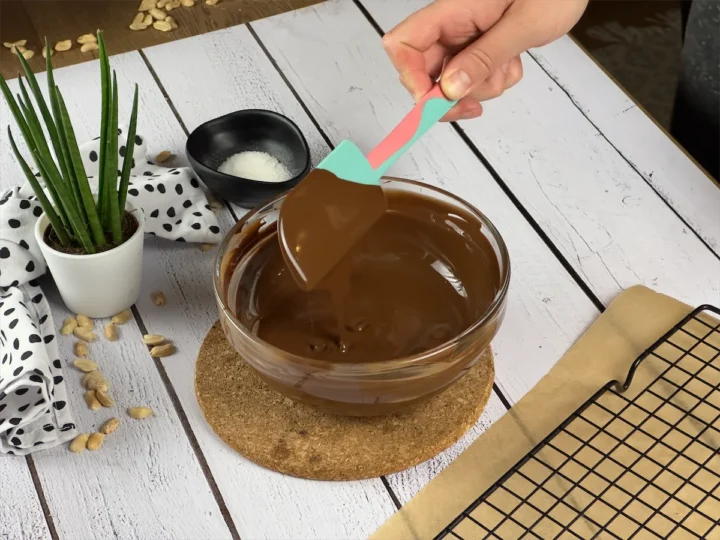 Spatula stirring melted dark chocolate in a bowl.