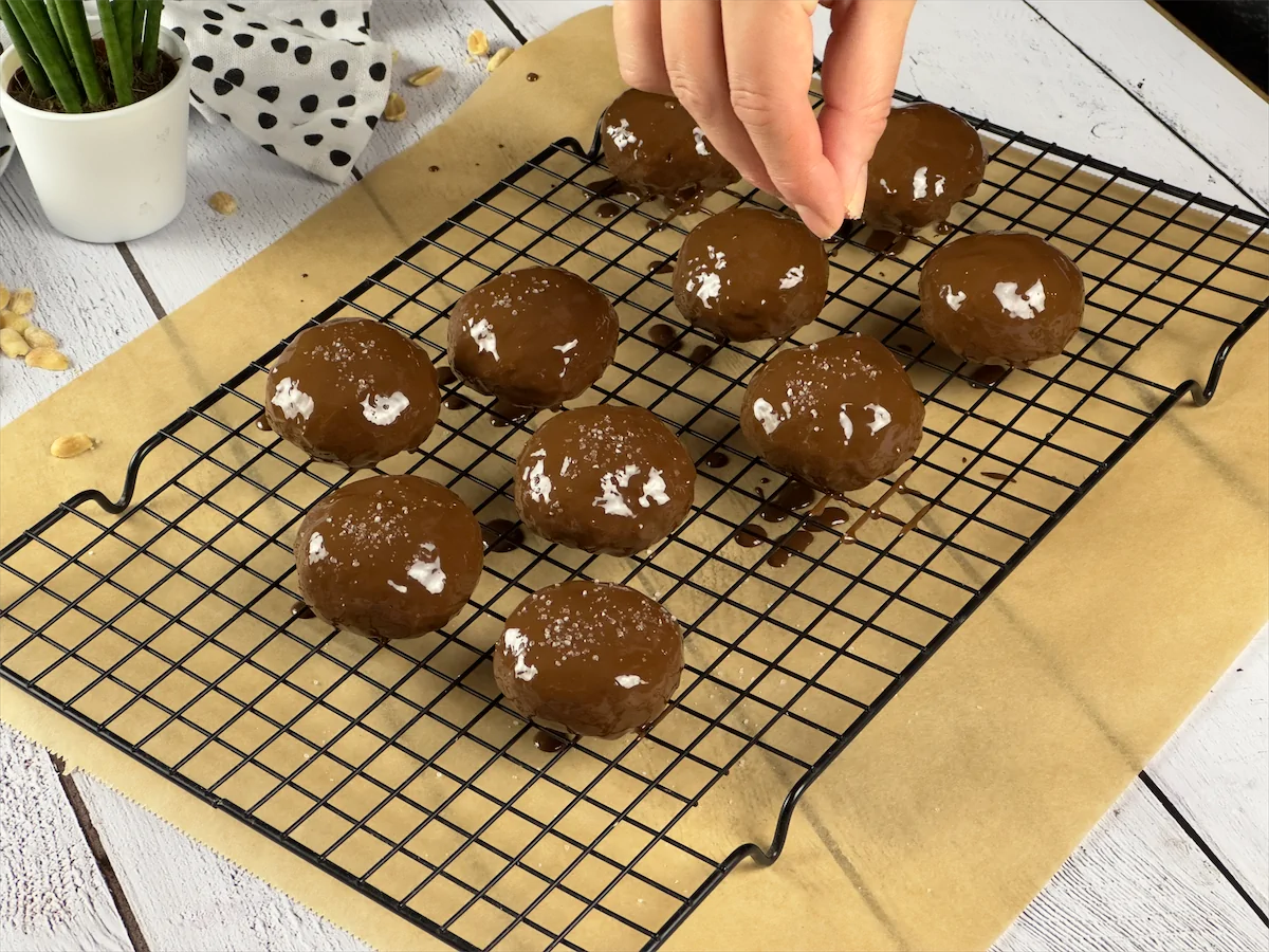 Chocolate-coated cookies being sprinkled with sea salt.