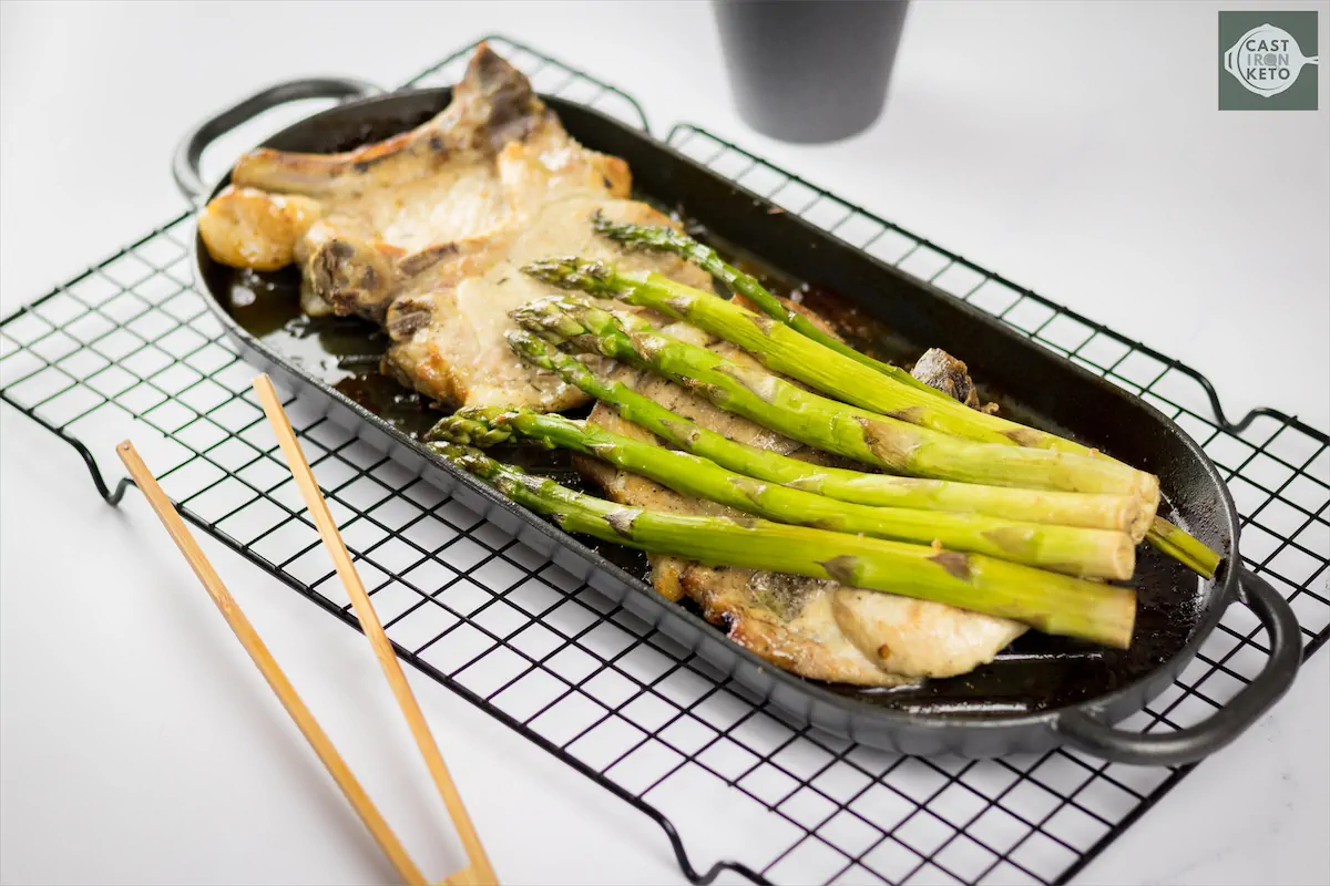 Keto baked pork chops served with asparagus on a cast iron baking dish.