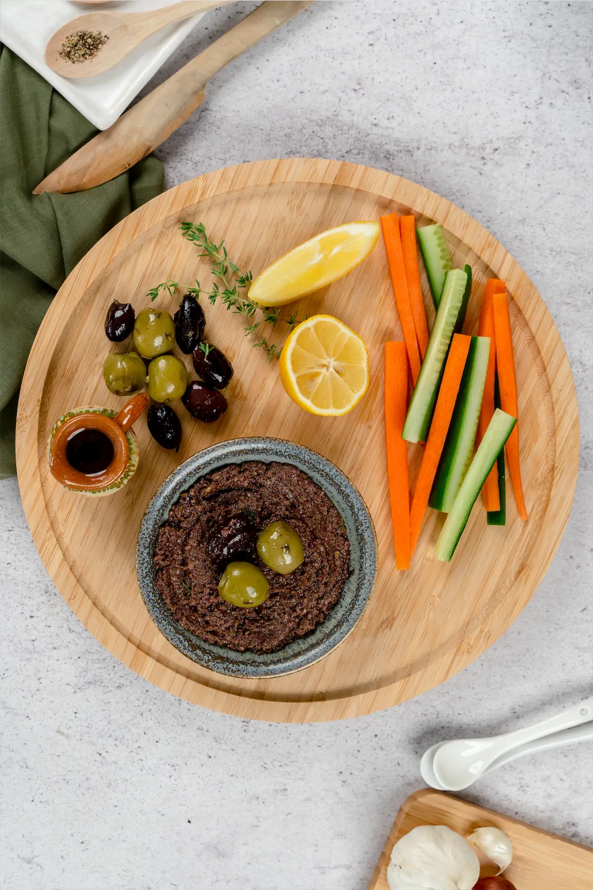 Classic Olive Tapenade served on a plate along with some olives, capers, sliced radish, sliced cucumbers and lemon.