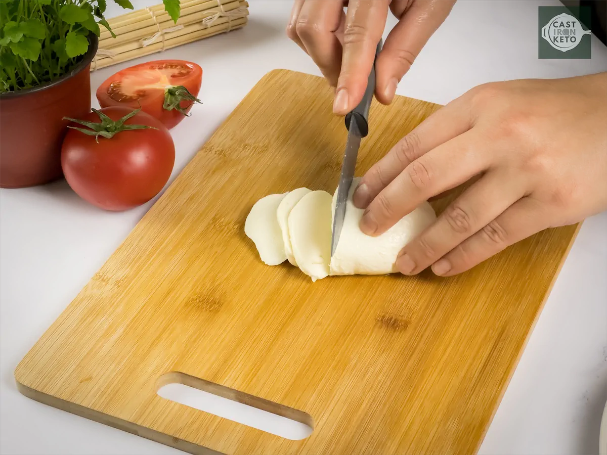Mozzarella being thinly sliced by a knife.