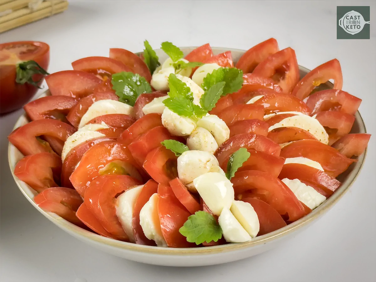 Freshly prepared bowl of caprese salad showcasing tomatoes, mozzarella, basil leaves and seasonings.