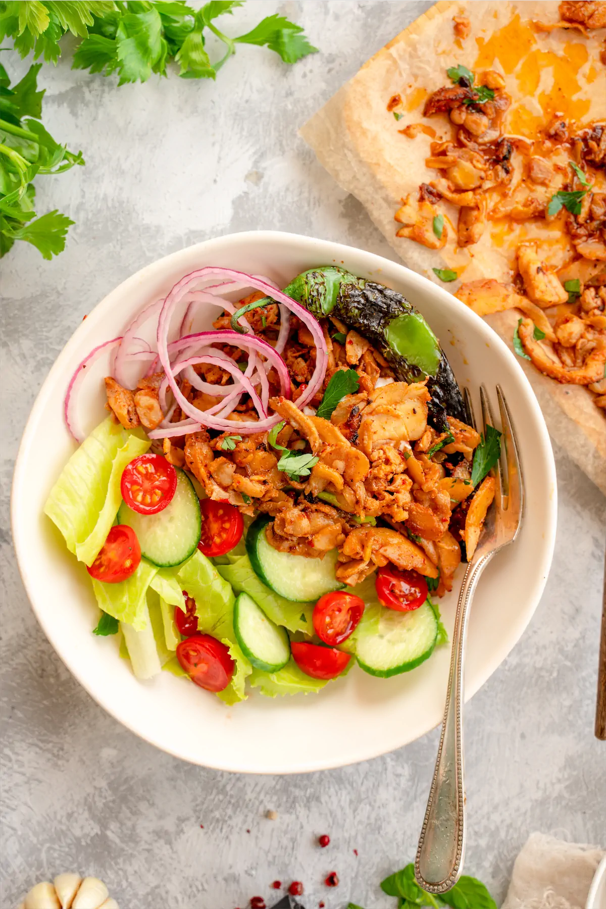 Chicken shawarma served with sliced cucumbers and cherry tomatoes in a bowl.