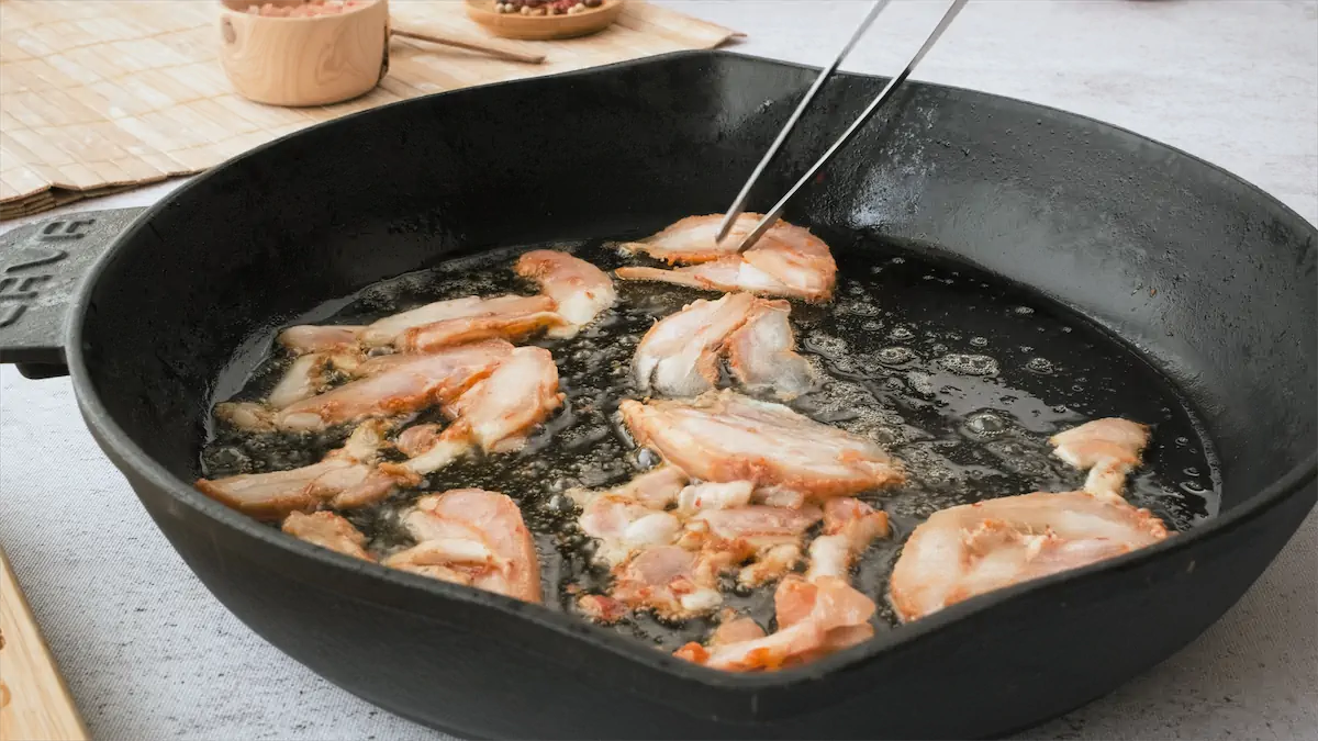 Cooking the marinated chicken slices in a cast iron pan.