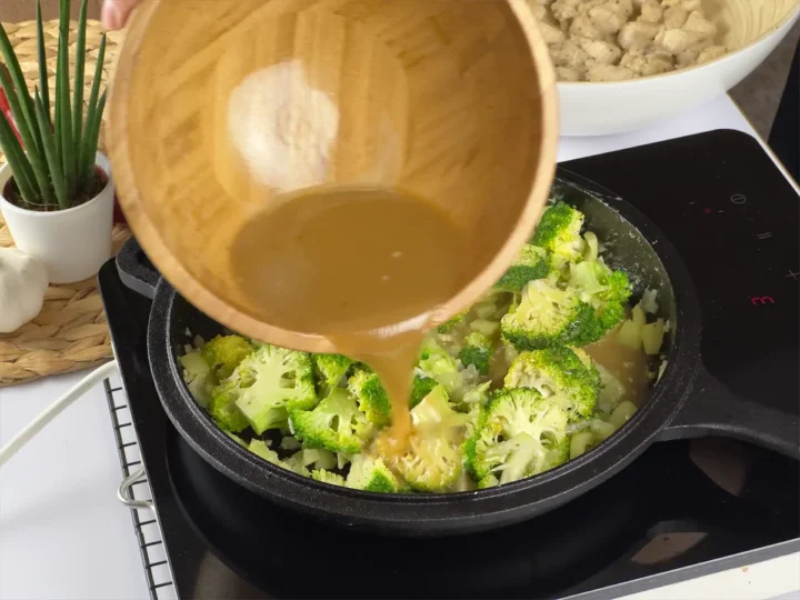 Adding sauce to the cast iron pan with broccoli, chicken and other veggies.
