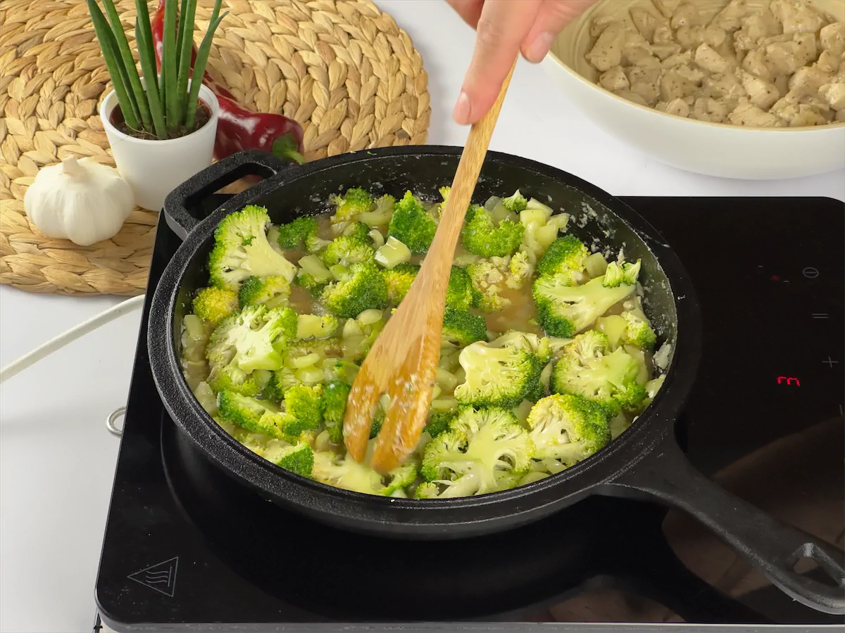 Sautéing vegetables in a cast iron pan with wooden spatula.