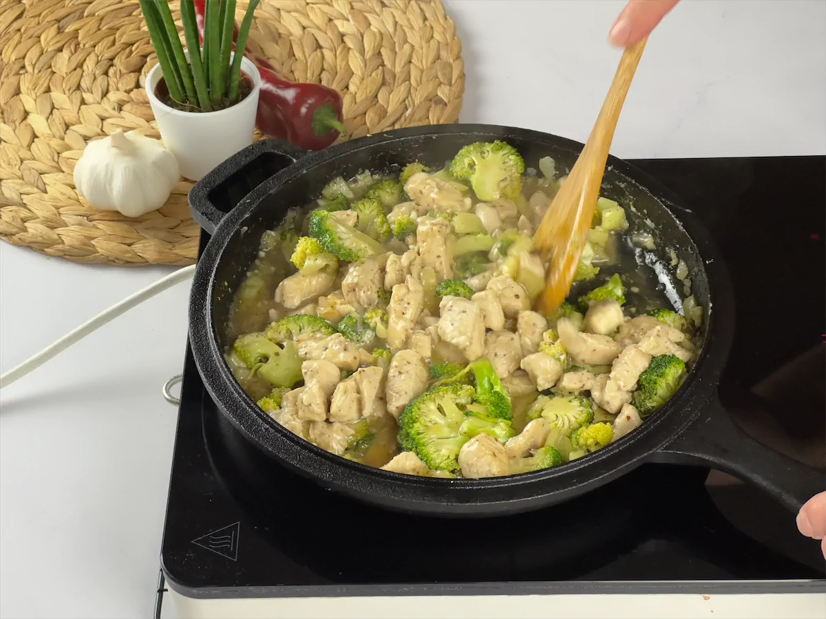 Adding chicken chunks to veggies in a cast iron dish.