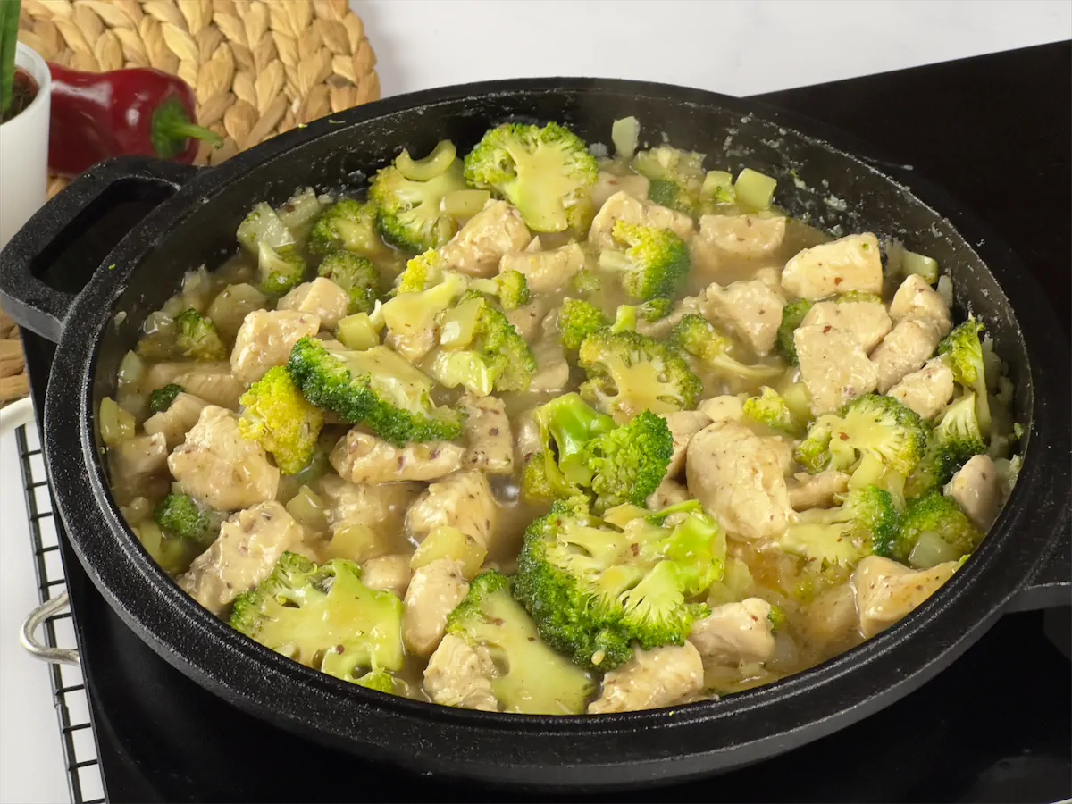 Chicken and broccoli being cooked in a cast iron dish.