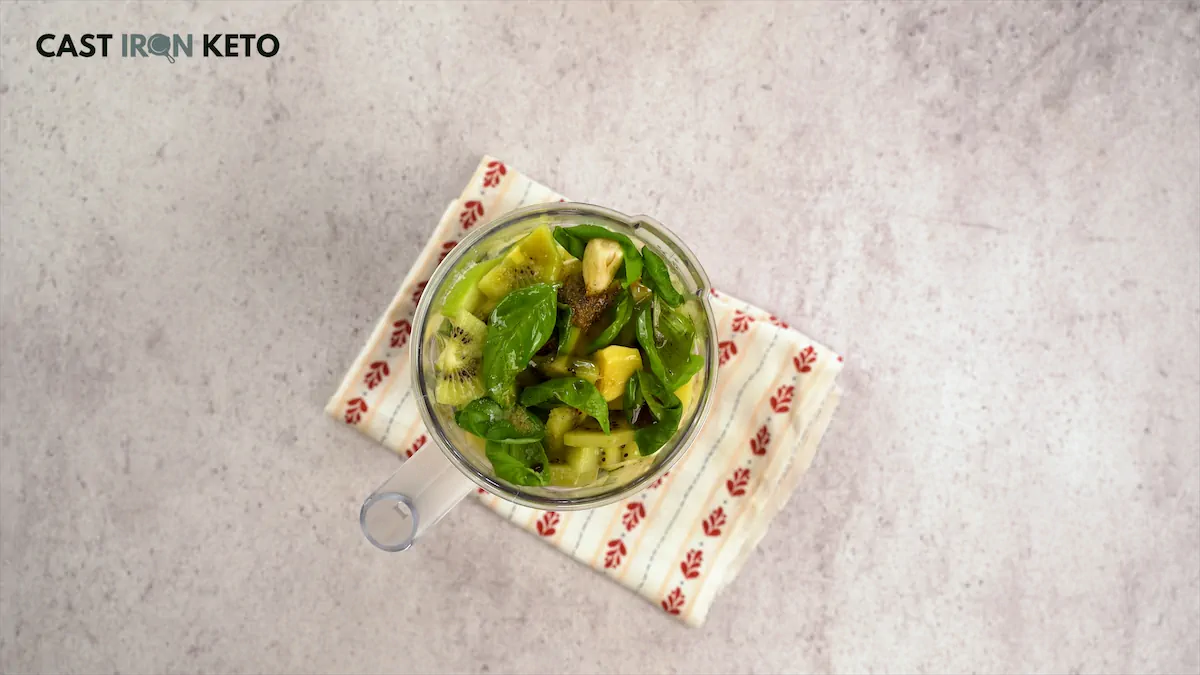 Chunks of cucumbers, apple, zucchini, and kiwi put together with basil, garlic, ginger, and spinach in a blender.